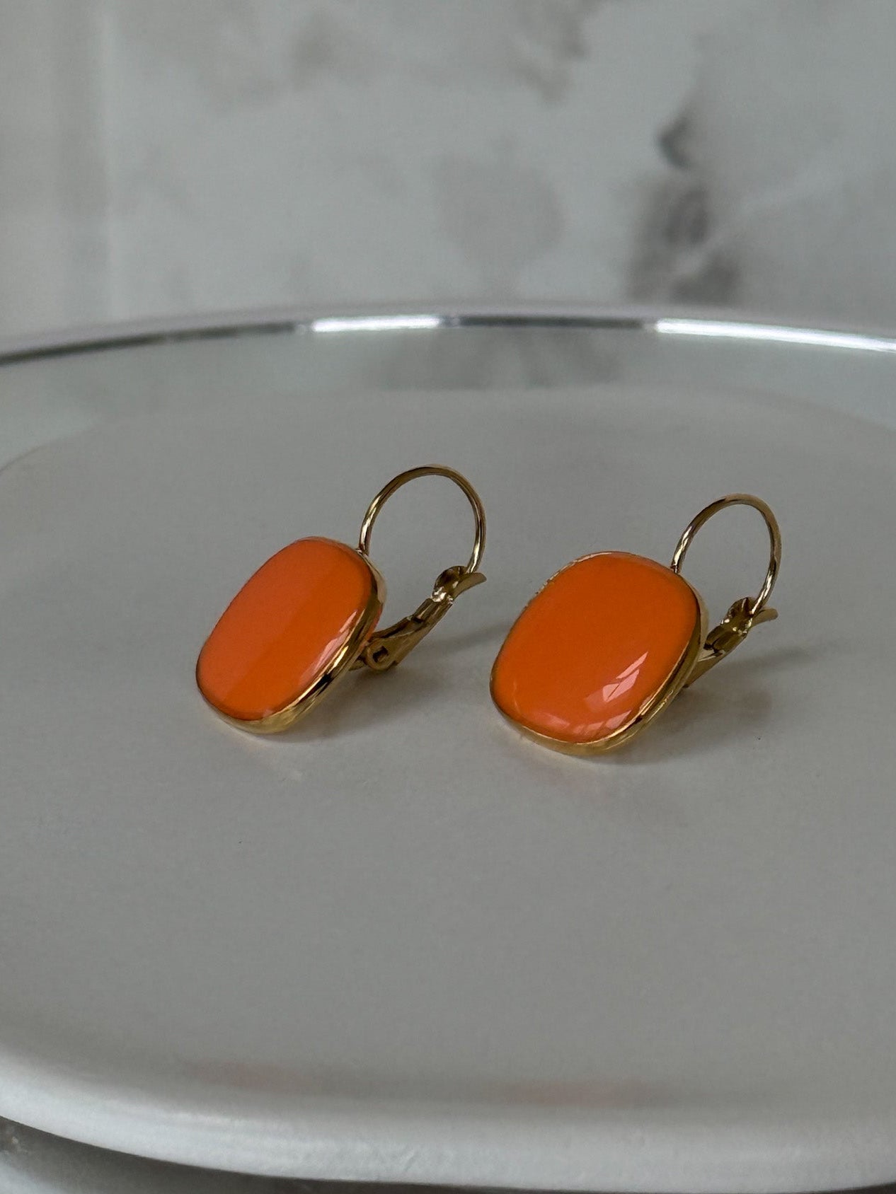 Orange earrings with gold hooks on a white plate