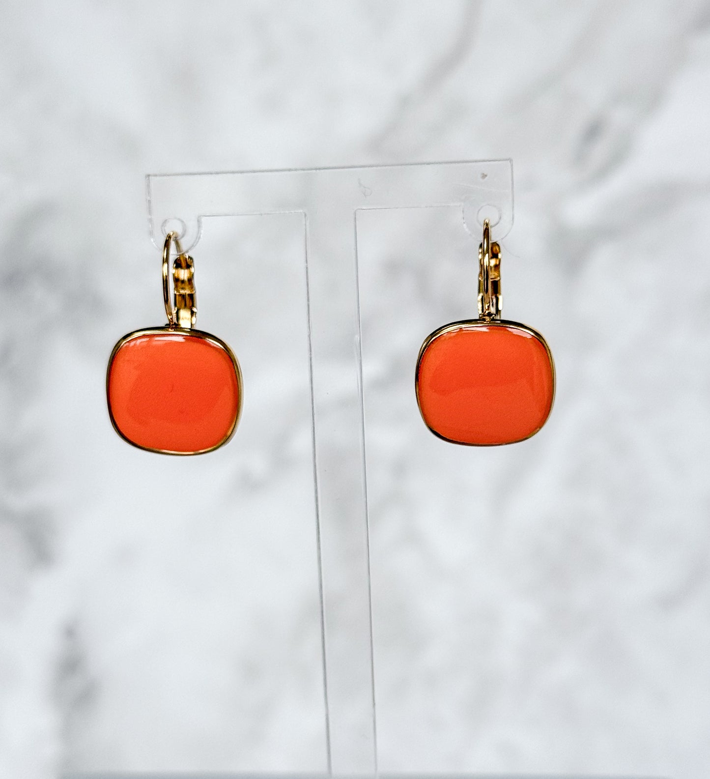 Orange square earrings on clear stands against a white background