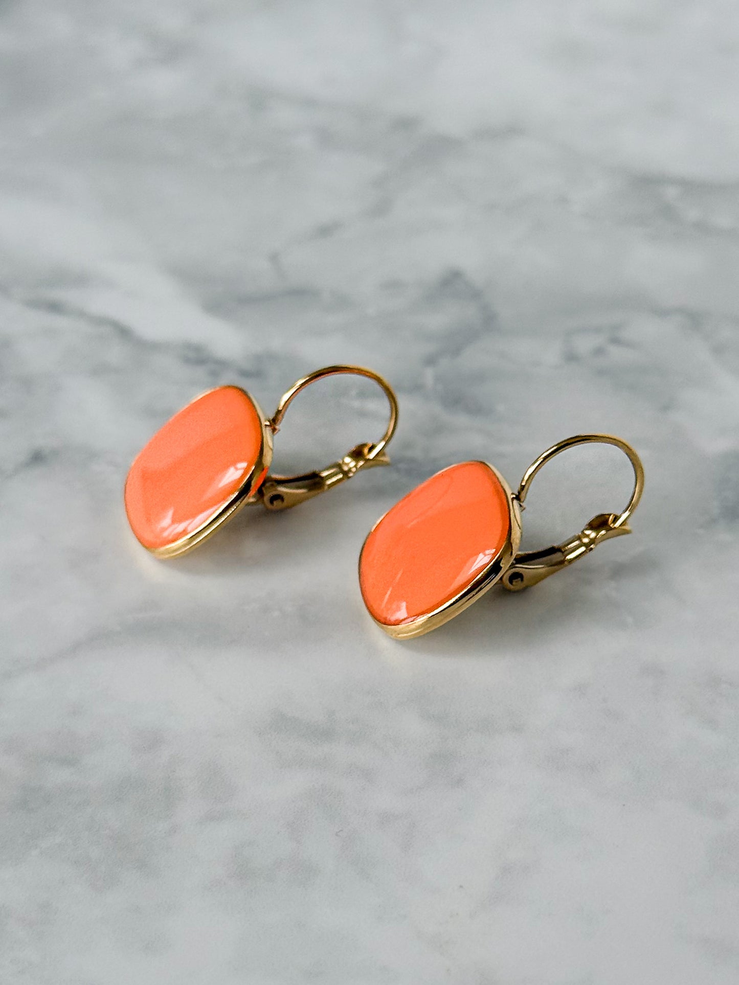 Orange earrings with gold hooks on a marble surface