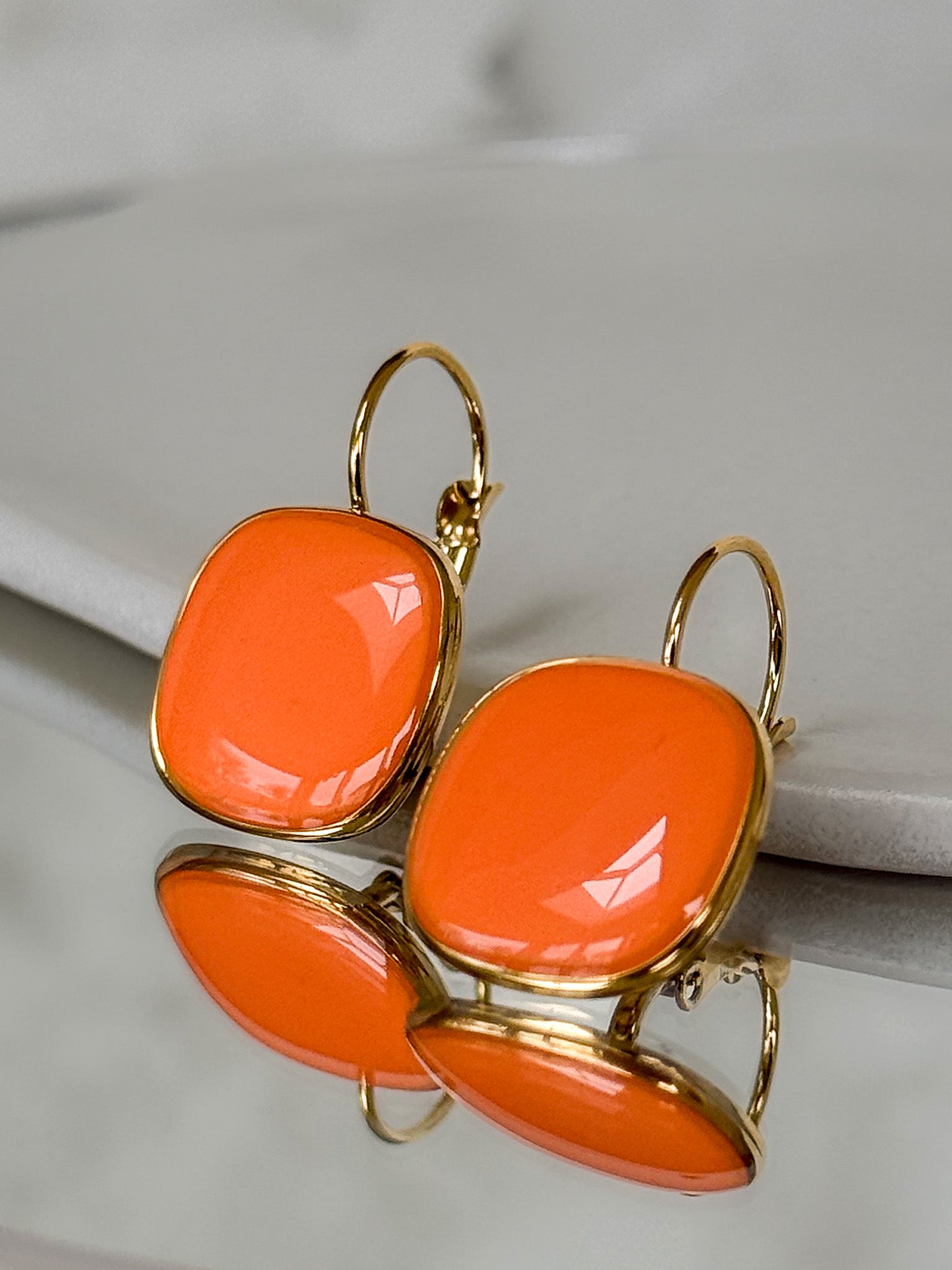 Orange earrings with gold frames on a light gray background