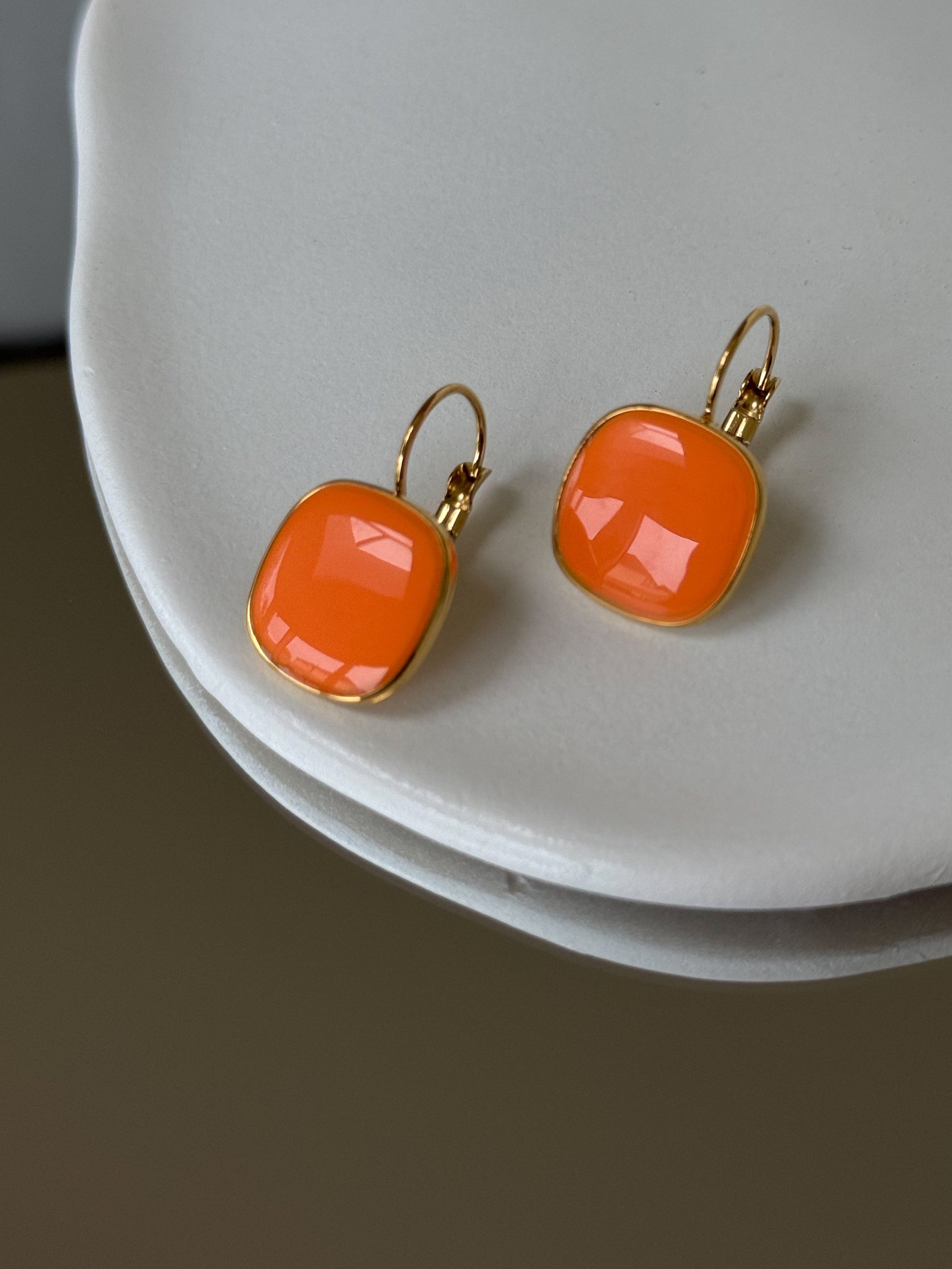 Orange earrings with gold frames on a white surface